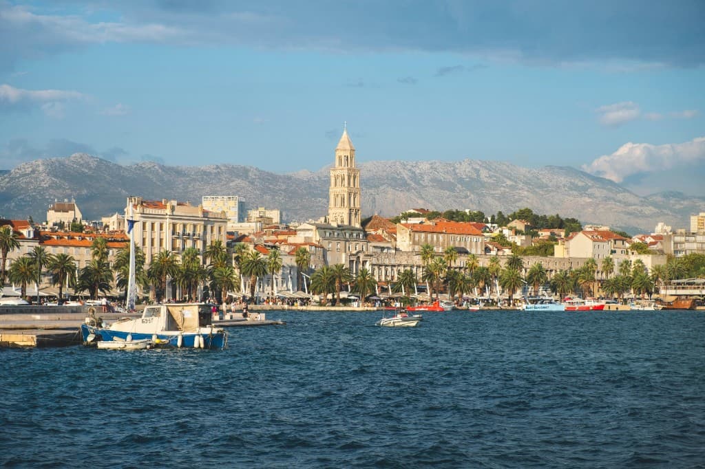 Split waterfront from the sea: Saint Domnius Cathedral bell tower, palm-lined Riva, Adriatic, and mountains