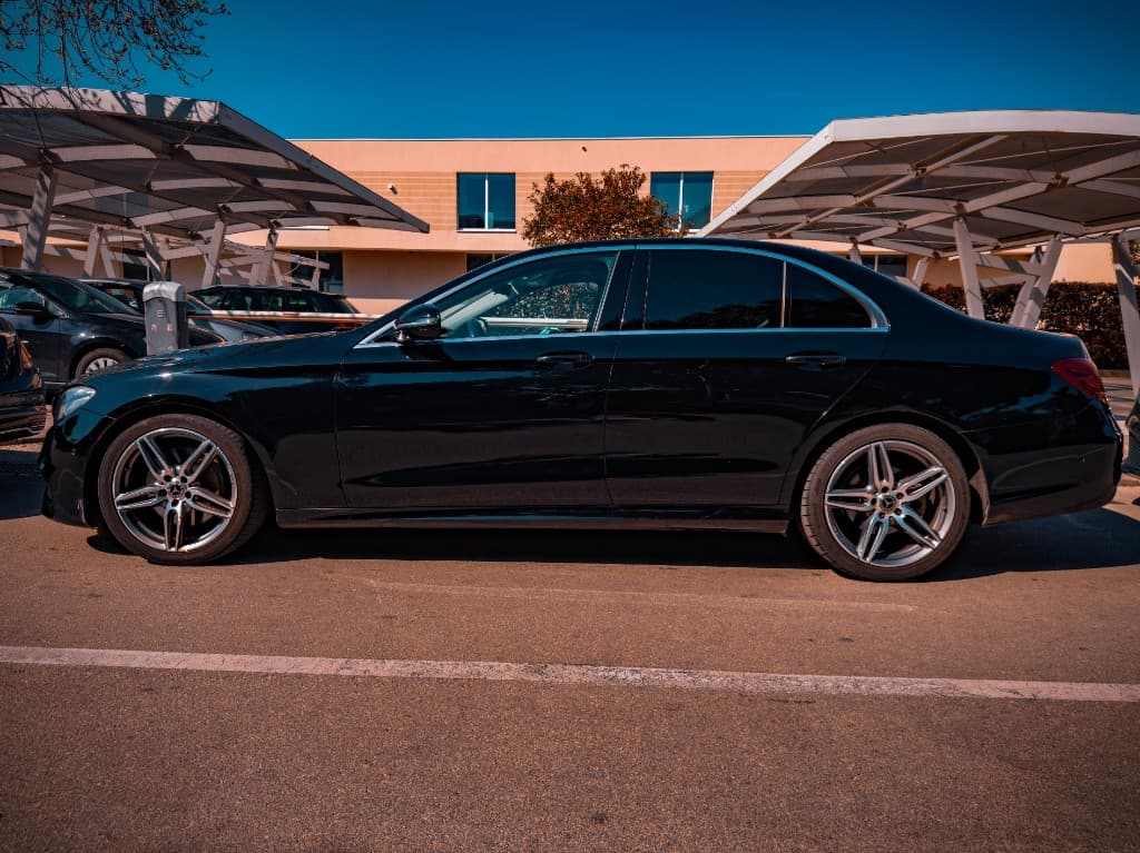 Black Mercedes-Benz E-Class side profile on an open lot under clear sky
