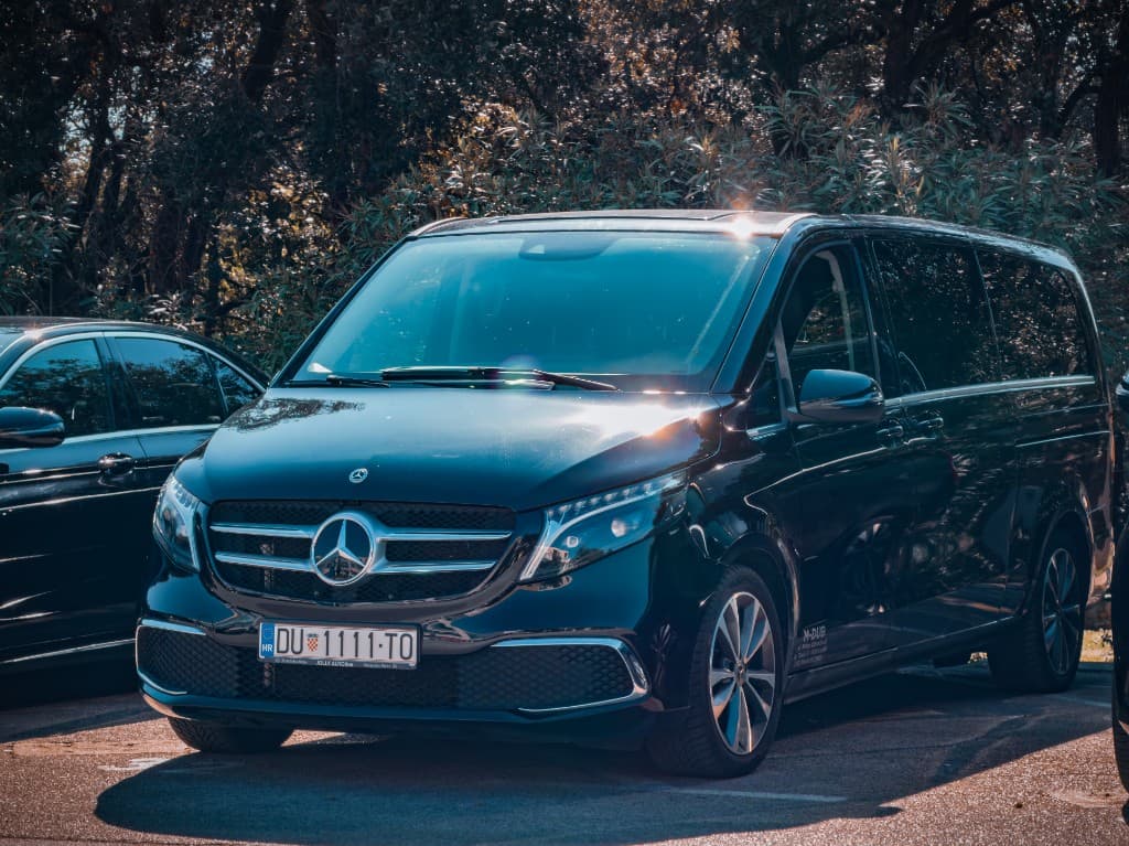 Black Mercedes-Benz V-Class van, front three-quarter view with trees behind